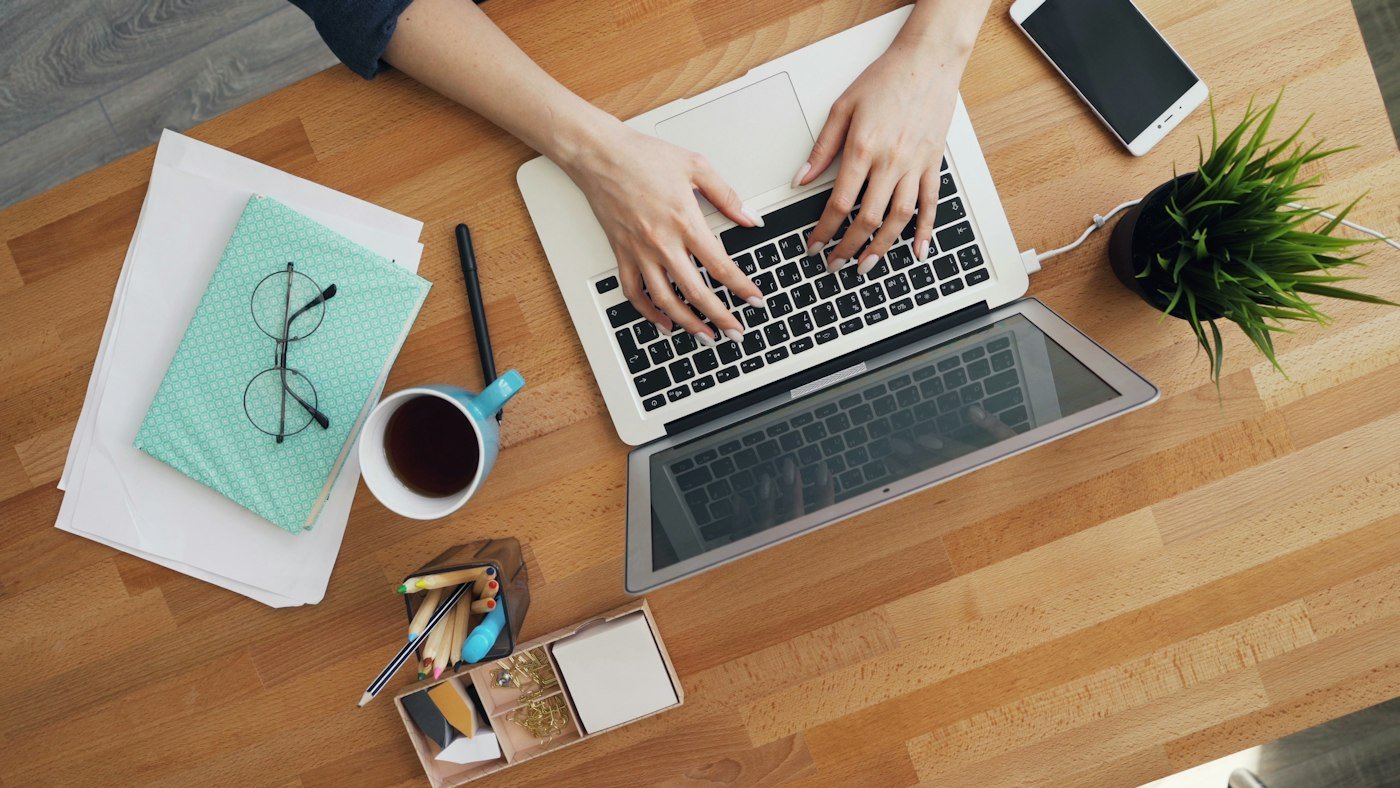 Hands at work on a laptop on a wooden desk, with a cup of tea and notes