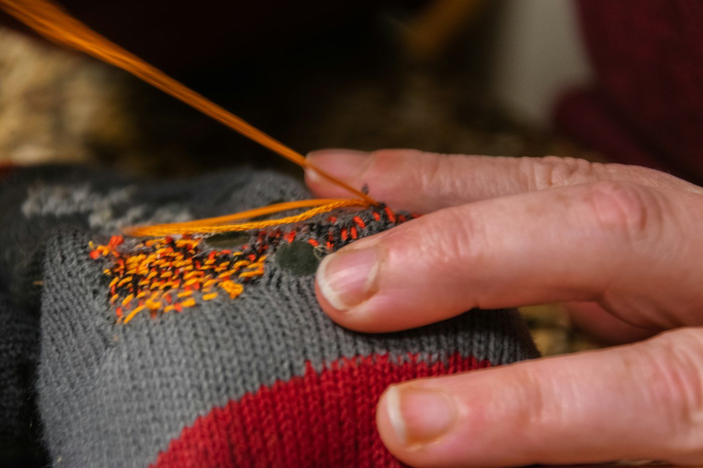 A hand darning a hole in a grey jumper with orange thread
