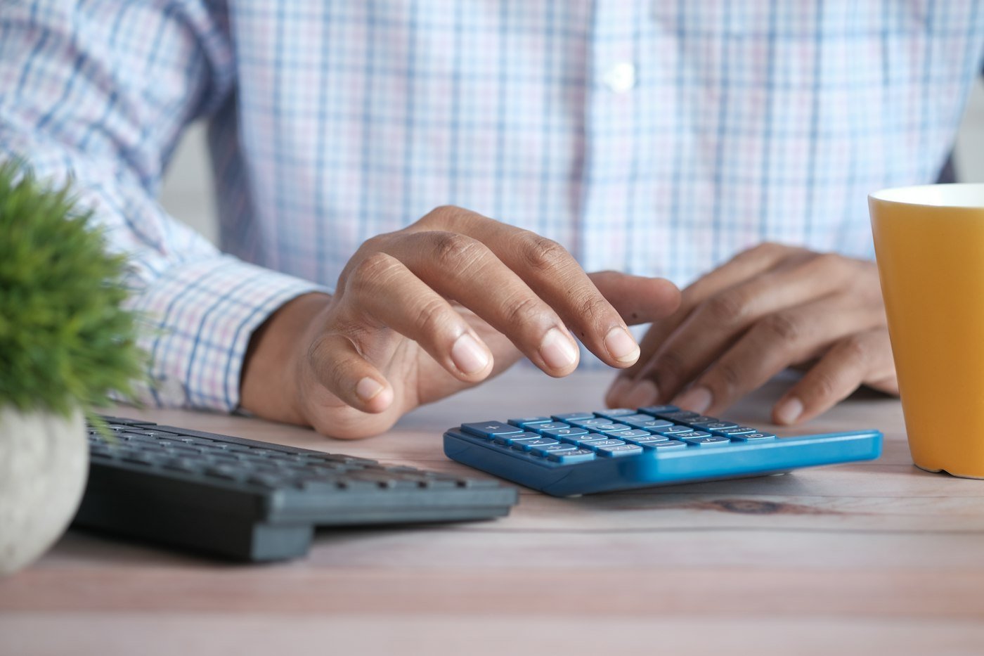 Hands adding up on a calculator beside a keyboard