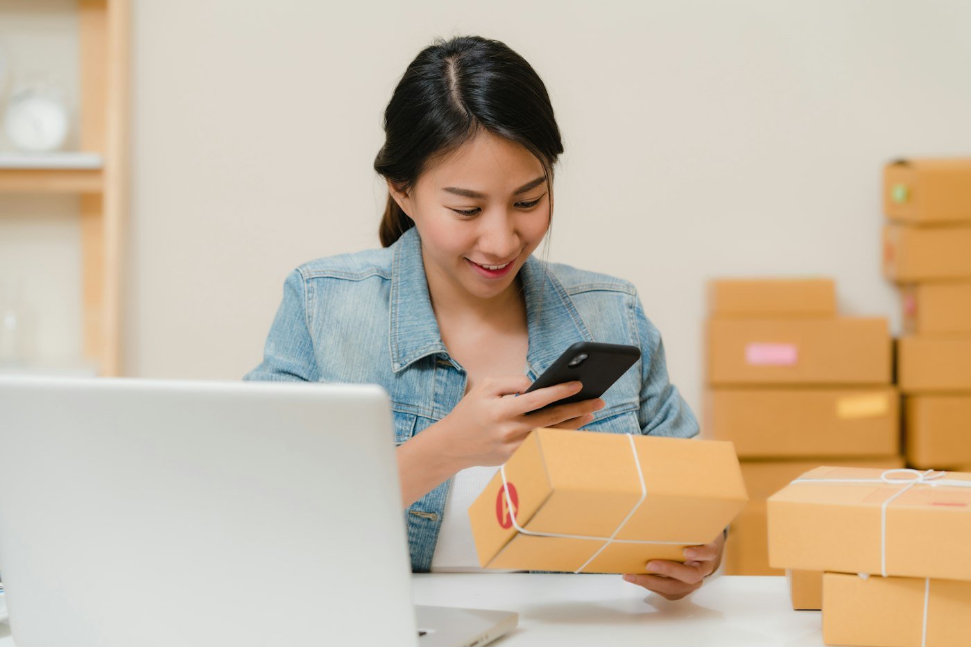 A small business owner checks an order on her phone beside parcels ready to post