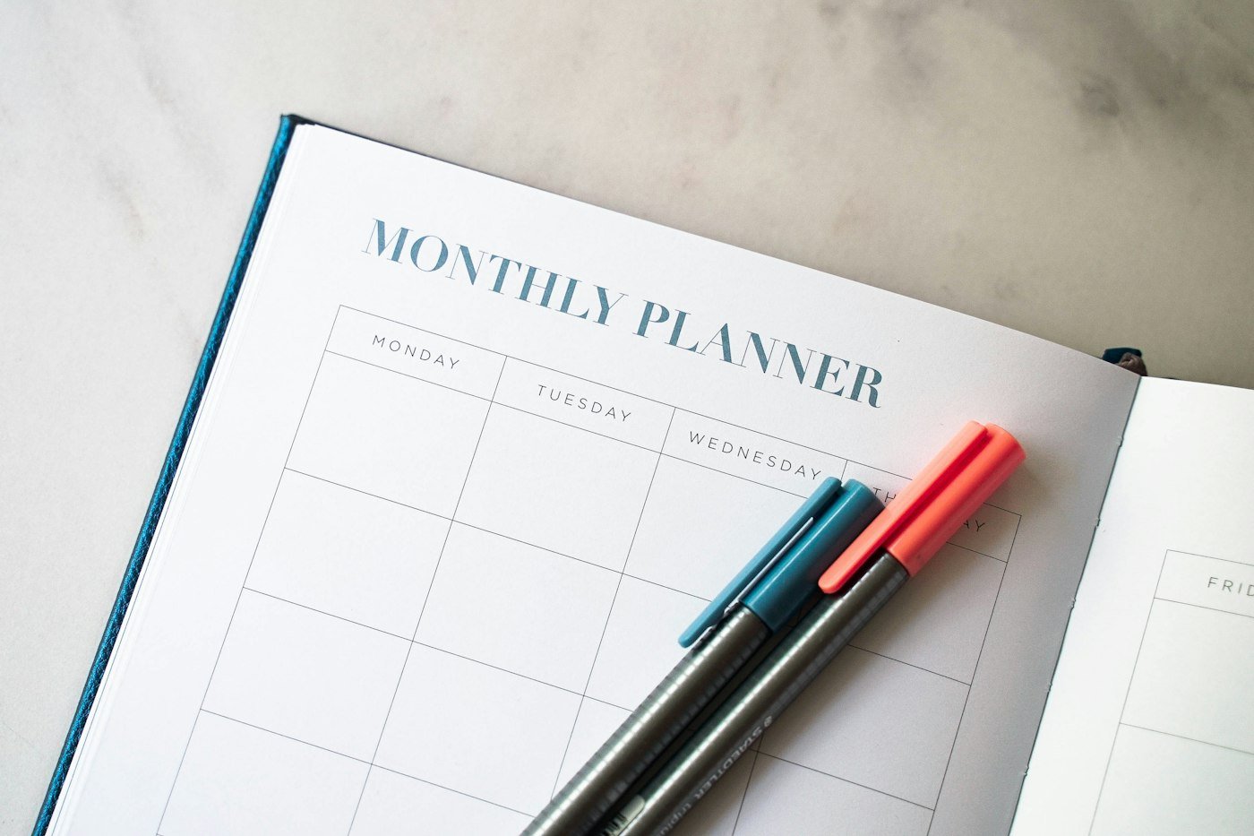 A monthly planner open on a desk with two pens