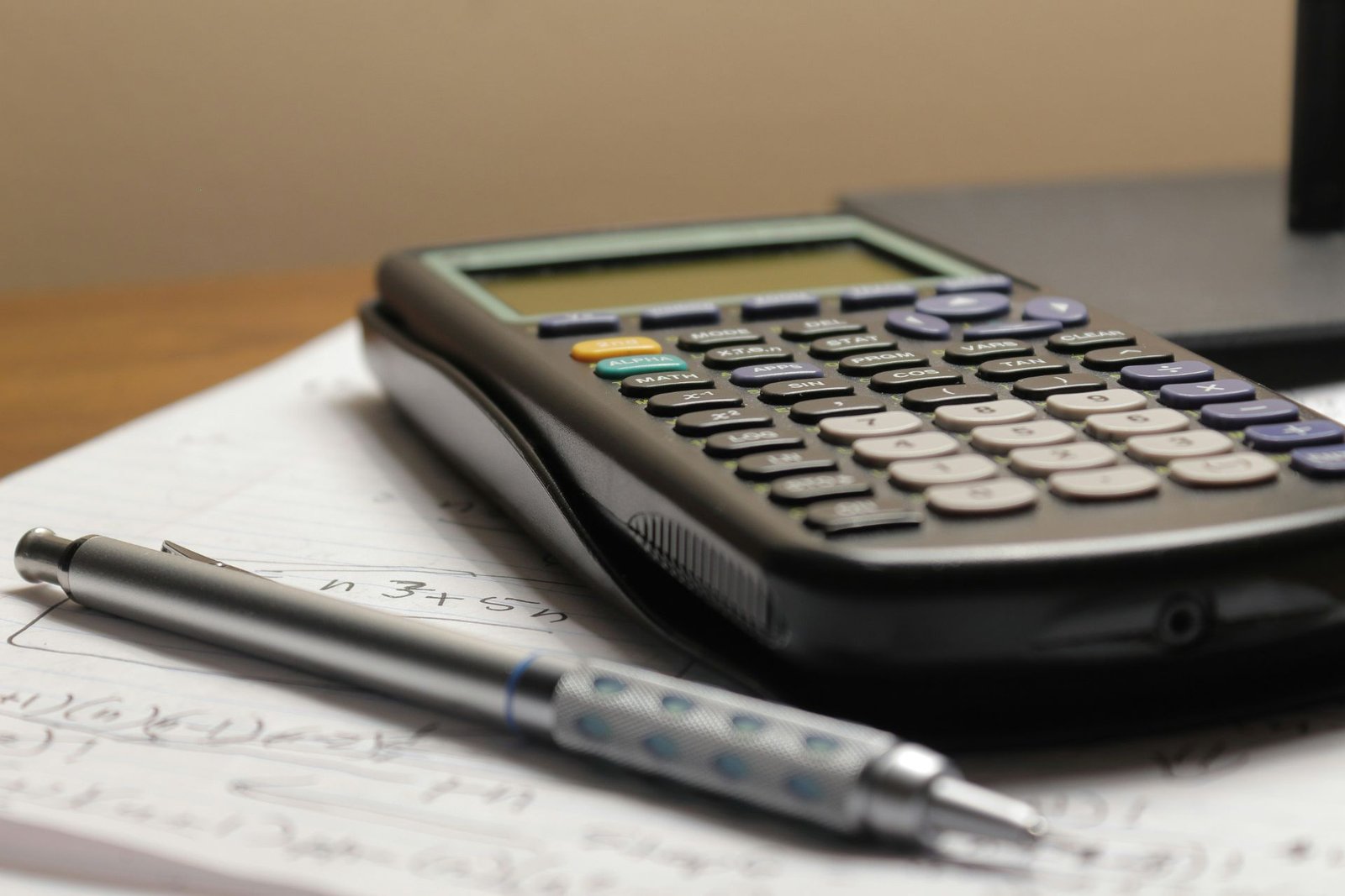 A calculator and a pen resting on a page of handwritten sums