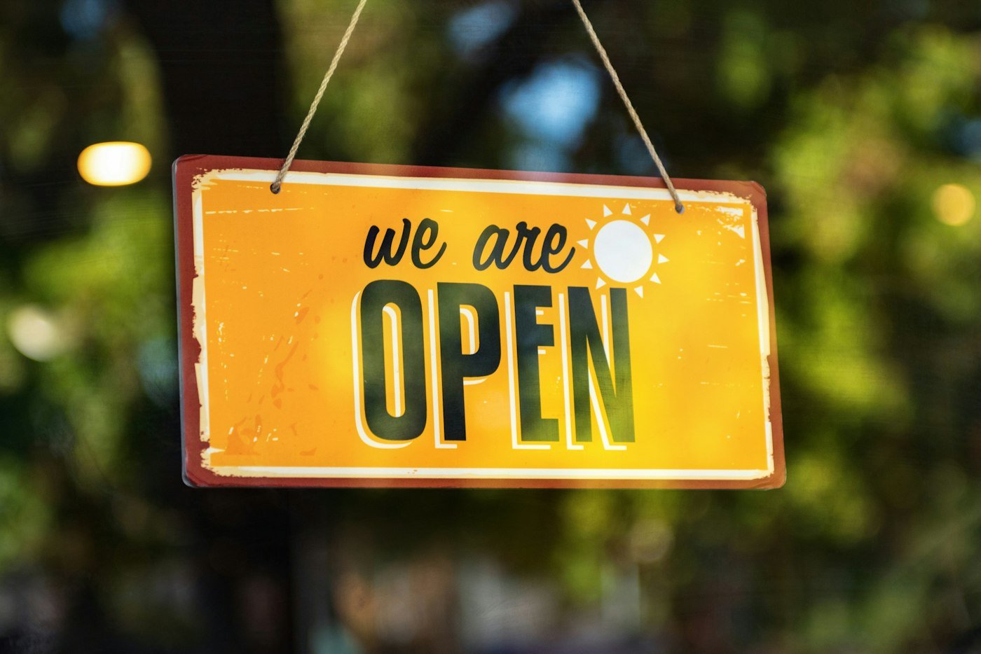 A hand painted we are open sign hanging in a shop window