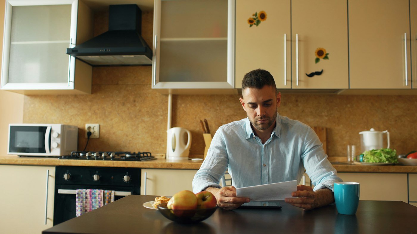 A man reading a letter at his kitchen table