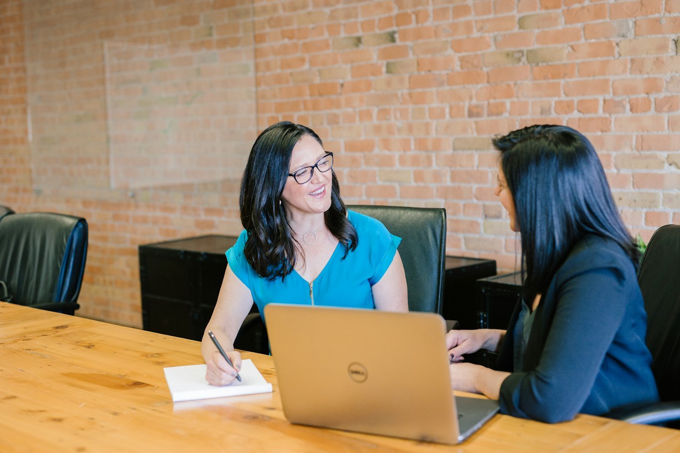 Two women talking across a table with a laptop between them