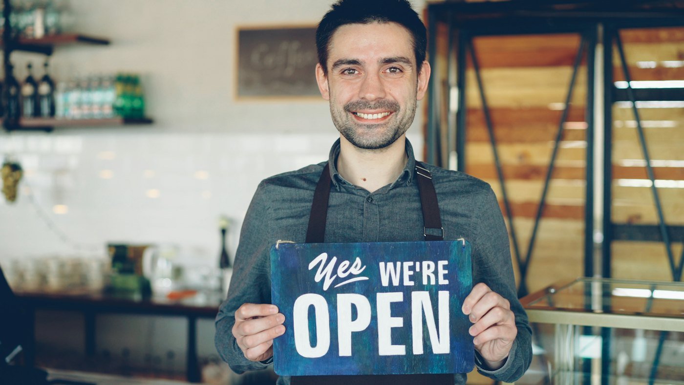 A shop owner holding up a sign that says yes, we are open