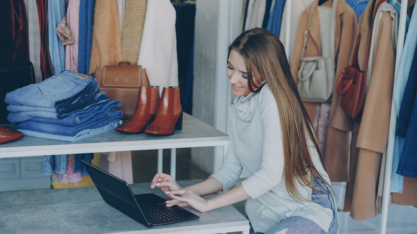 A boutique owner working on her laptop among the clothes rails
