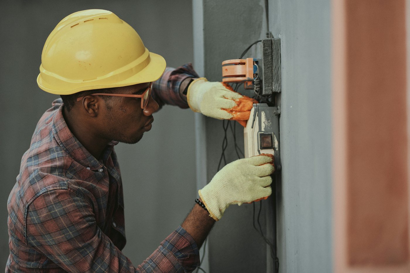 An electrician in a hard hat fitting a socket to a wall