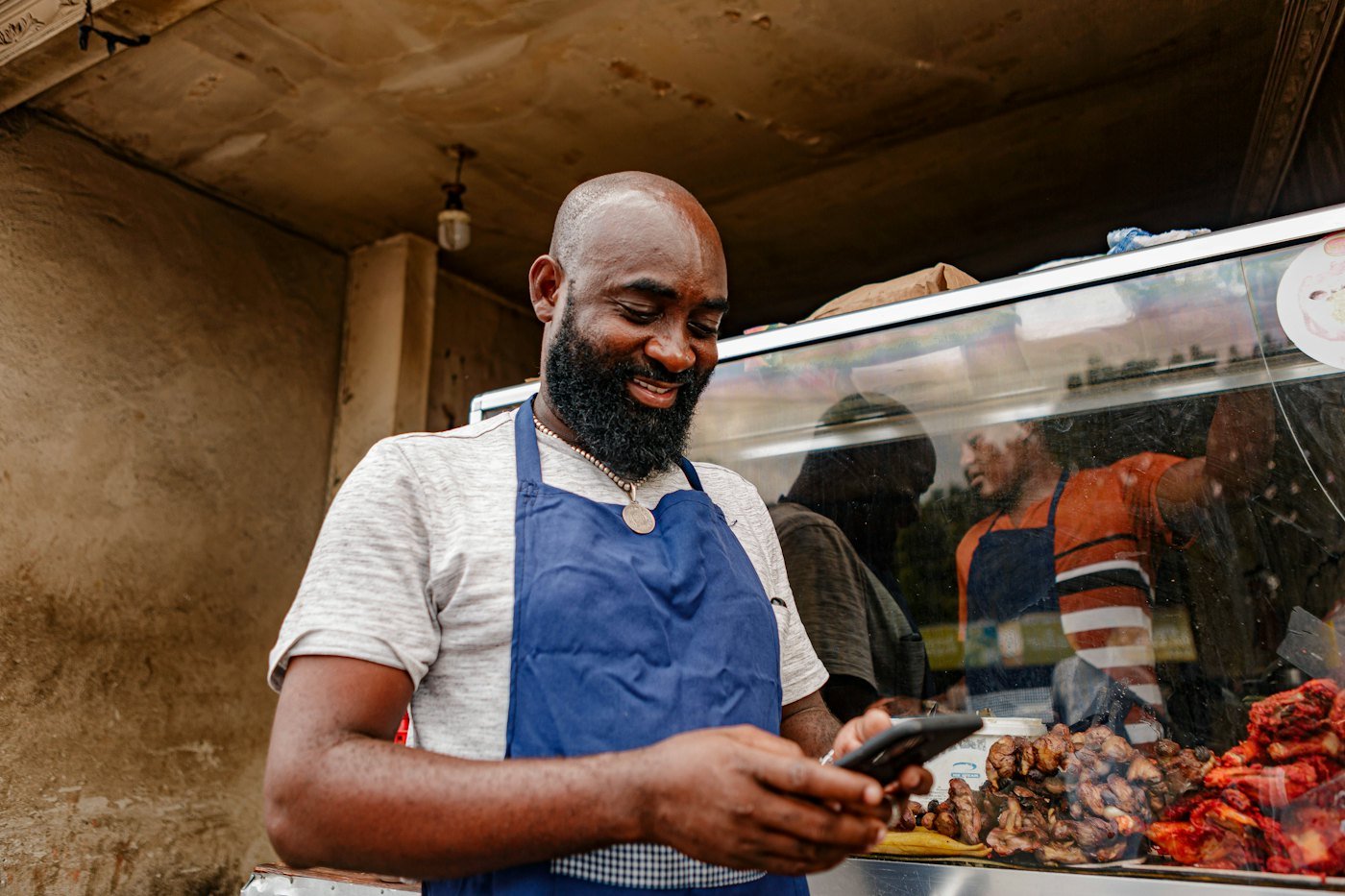 A market stallholder in a blue apron checking his phone at his stall
