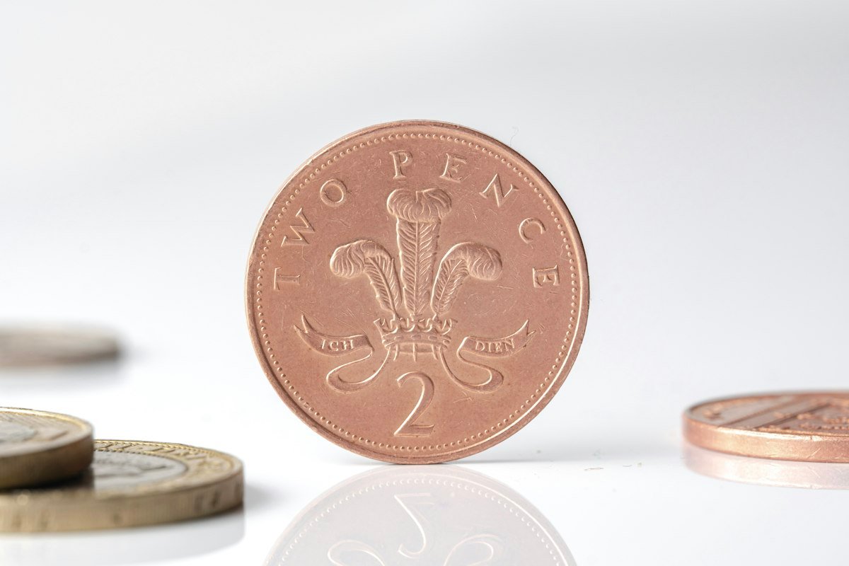 A British two pence coin standing on edge in front of other coins