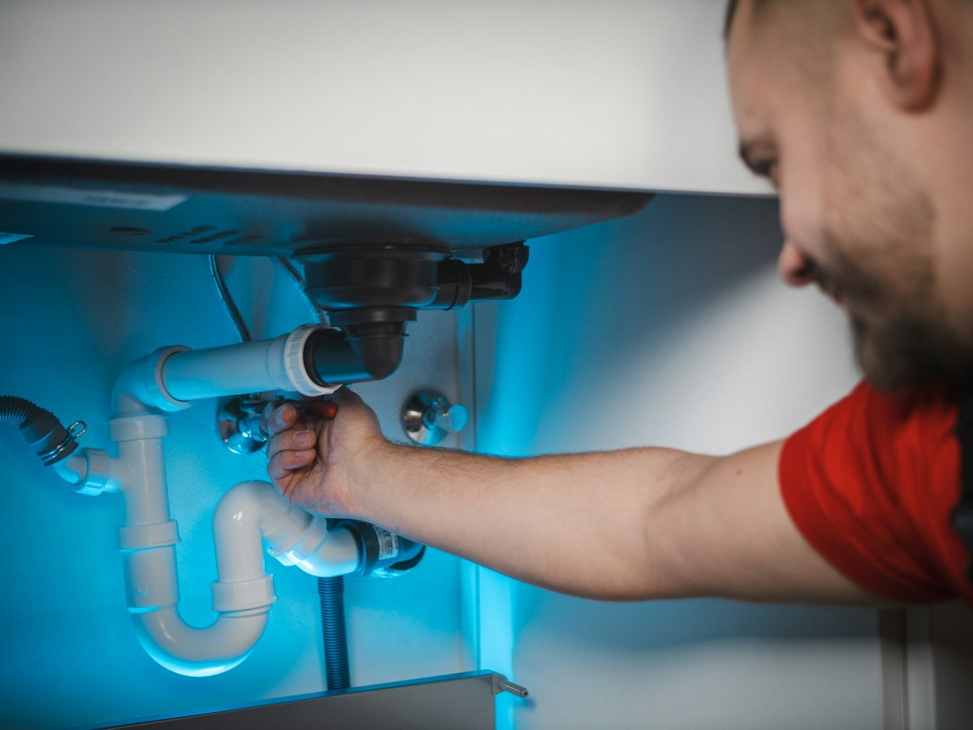 A plumber fitting pipework under a sink